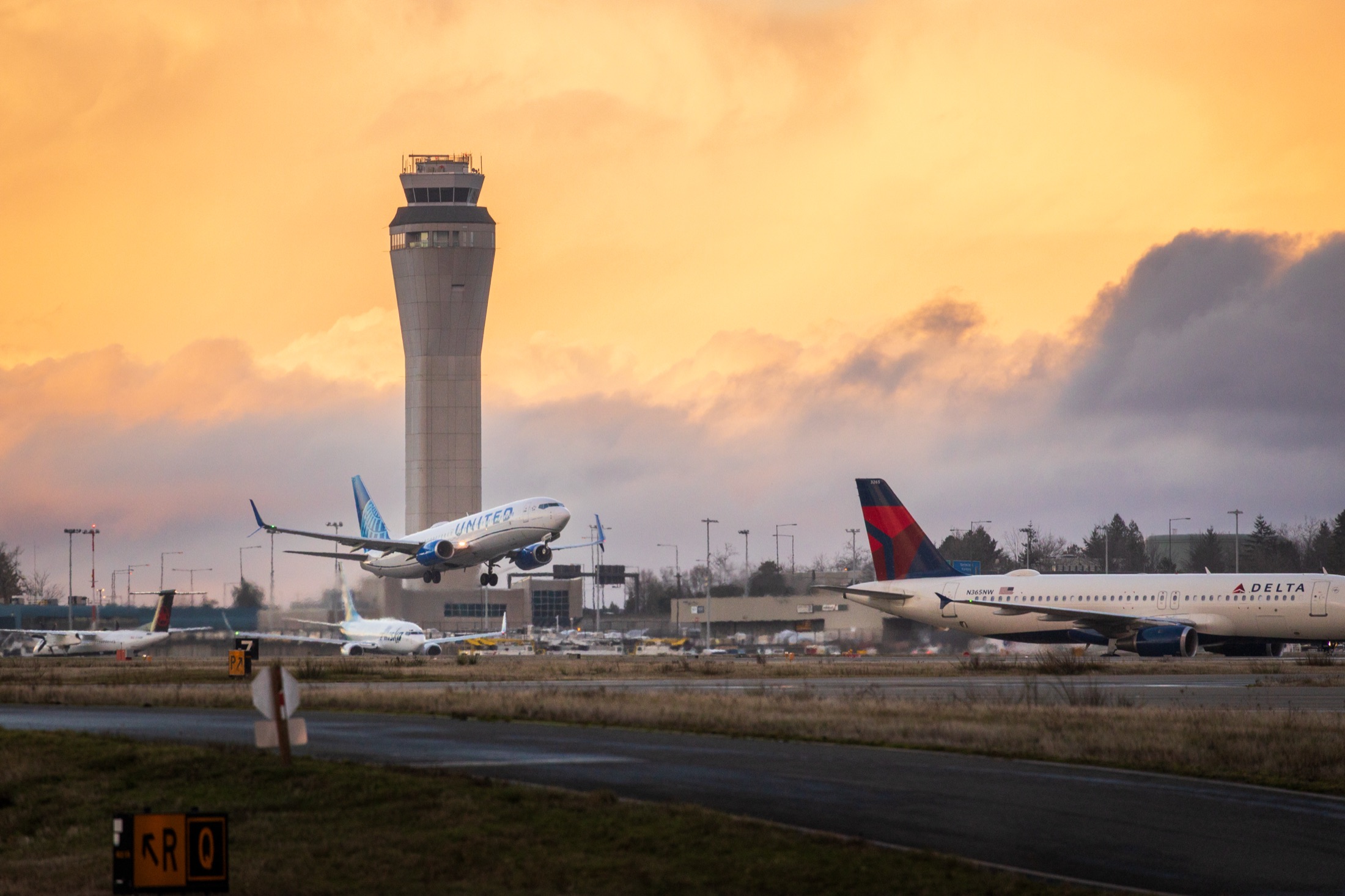 A United Boeing 737-800 rotating off the runway at Seattle–Tacoma International at sunset, with the control tower behind it